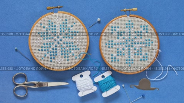 Video of two hand embroidered cross stitch snowflakes in hoops on blue background and accessories for cross stitch. Winter crafts and Christmas gifts concept. Cross stitches as hobby. Flat lay, close-up. Стоковое видео, видеограф Виктория Катьянова / Фотобанк Лори