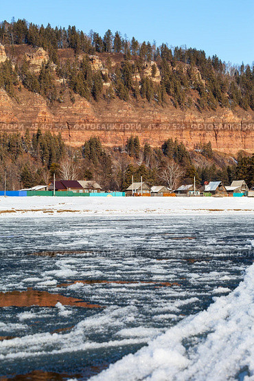 View of Siberian village of Shamanka near beautiful Shamansky cliff on bank of Irkut River in November during freeze-up of river. Сliff is natural landmark of Irkutsk region and place for tourists to travel. Стоковое фото, фотограф Виктория Катьянова / Фотобанк Лори
