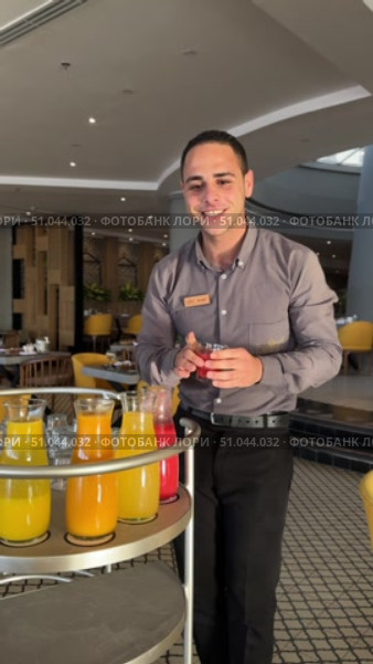 Waiter serving beverages at an upscale restaurant Pouring fresh orange juice!Waiter serving hotel guests during breakfast Portrait of cheerful waiter holding a tray with orange juices looking at camera smiling. Редакционное видео, видеограф Zita Khasanova / Фотобанк Лори