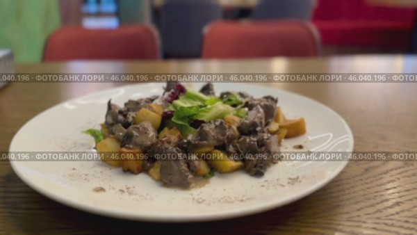 Warm salad with chicken liver in cream sauce with fried potatoes, mushrooms and mixed green salad in a white porcelain plate on a brown wooden table in an elite restaurant. Стоковое видео, видеограф worker / Фотобанк Лори