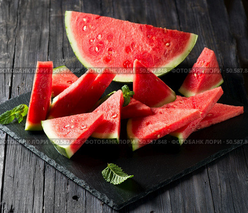 Watermelon slices and half decorated with mint on a black slate board. Стоковое фото, агентство Ingram Publishing / Фотобанк Лори