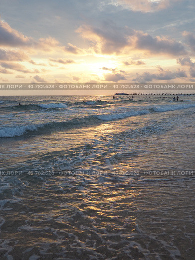 Wave and sunset over sea. Beautiful sunset. Foamy waves roll over the sandy shore. Vityazevo, Anapa, Black Sea. Tourist mecca, health resort. Evening sky. The rays reflect off the water. Стоковое фото, фотограф Юлия Петровская / Фотобанк Лори