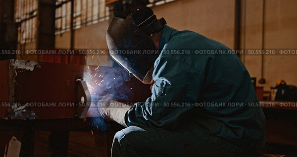 Welder in protective uniform and mask welding metal pipe on the industrial table while sparks flying. Стоковое фото, агентство Ingram Publishing / Фотобанк Лори