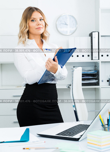 Well-wishing girl with folder of documents is standing in well-lit office. Стоковое фото, фотограф Яков Филимонов / Фотобанк Лори