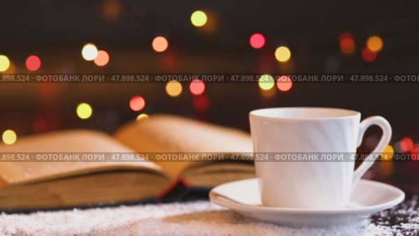 White cup and saucer and an old open book on a dark wooden table covered with snow. Стоковое видео, видеограф Zakharova Natasha / Фотобанк Лори
