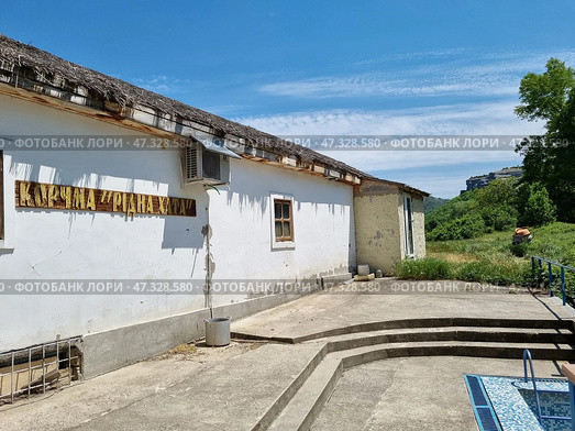 White plastered walls, a thatched roof (or imitation of it), simple wooden windows, an air conditioner on the wall — all this creates an atmosphere of rural comfort and authenticity.In the background are green hills, forest and mountains, which give the place privacy and natural beauty. Probably, this place is somewhere in Crimea or in the south of Ukraine, not far from tourist routes and attractions. Стоковое фото, фотограф Анна Кривицкая / Фотобанк Лори