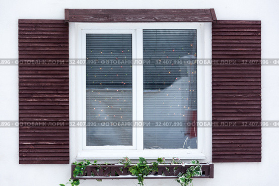 White plastic pvc window with decorative wooden shutters and Christmas lights inside, outdoor facade. Стоковое фото, фотограф Кекяляйнен Андрей / Фотобанк Лори