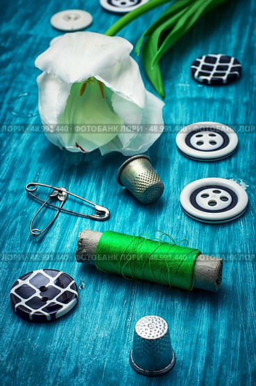 white tulip and buttons for clothing on light blue wooden background.the image is tinted in vintage style. thread and buttons. Стоковое фото, агентство Ingram Publishing / Фотобанк Лори