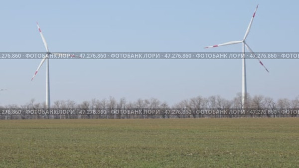 Wind turbines spin energetically against a blue sky, harnessing renewable energy in the countryside field on spring. Supporting farmers through innovative practices. Green and renewable power concept. Стоковое видео, видеограф Ирина Михайличенко / Фотобанк Лори