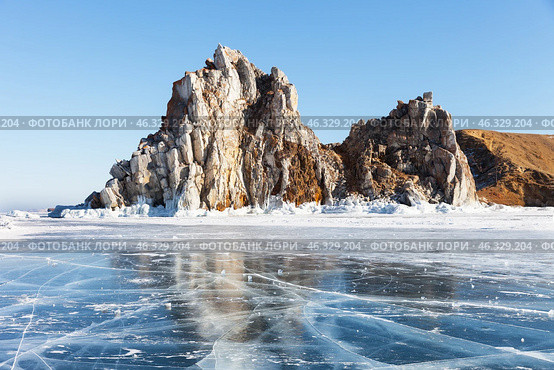 Winter landscape of frozen Baikal Lake with famous Shamanka rock - natural landmark Olkhon Island from blue clear ice with cracks on sunny day in February. Cape Burkhan - place of attraction for tourists. Стоковое фото, фотограф Виктория Катьянова / Фотобанк Лори