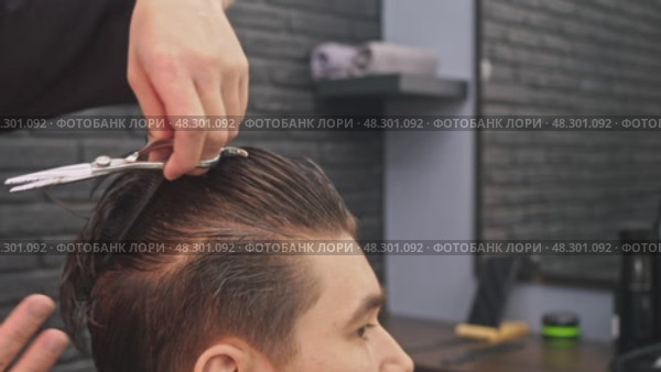 With skilled and precise movements, the experienced barber carefully cuts the ends of the young male client's hair. Стоковое видео, видеограф Strunov David / Фотобанк Лори