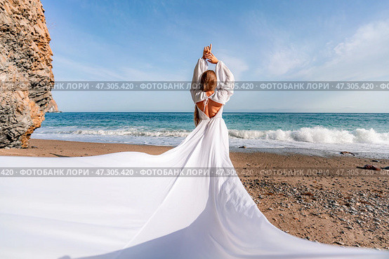 Woman beach white dress flying on Wind. Summer Vacation. A happy woman takes vacation photos to send to friends. Стоковое фото, фотограф svetograph / Фотобанк Лори