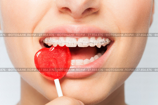 Woman bites off red lollipop in the shape of heart. Стоковое фото, фотограф Сергей Новиков / Фотобанк Лори