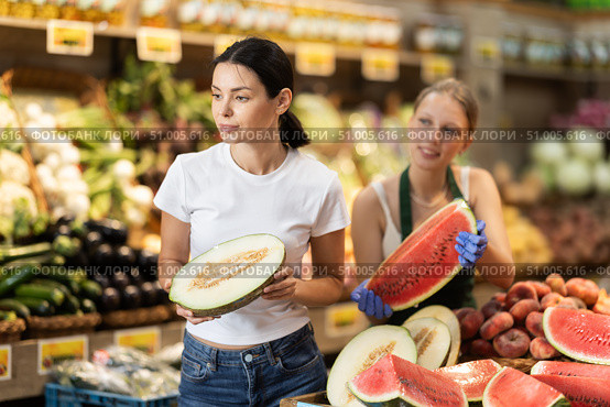 Woman customer in vegetable store examines melon, female seller help. Стоковое фото, фотограф Яков Филимонов / Фотобанк Лори