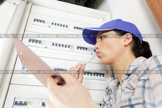woman electrician inspecting fuseboard holding clipboard. Стоковое фото, агентство Ingram Publishing / Фотобанк Лори