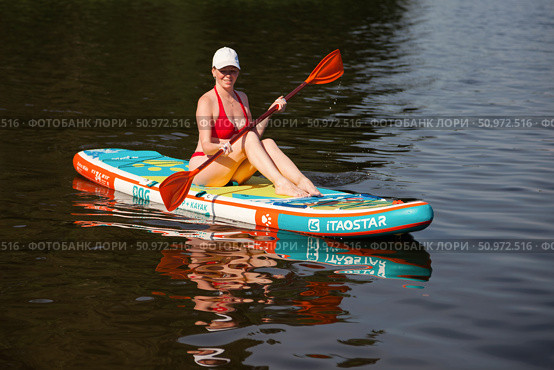 Woman Enjoying Stand-Up Paddleboarding on a Serene Lake Surrounded by Peaceful Nature. Редакционное фото, фотограф Aleksandr Golubev / Фотобанк Лори
