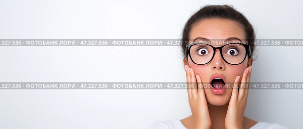 Woman expressing surprise with wide eyes and hands on her face, copy space. Молодая женщина в очках демонстрирует драматическое выражение удивления. Она стоит на простом белом фоне и выглядит потрясенной, с широко раскрытыми глазами и прижатыми к щекам руками. Стоковое AI-изображение, AI-художник Katsiaryna Repich / Фотобанк Лори