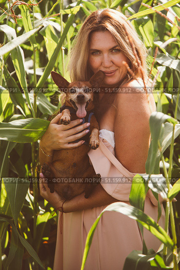 Woman gently holds her dog's head and leans in to kiss the dog s open mouth in a sunny grassy field under a bright sky, capturing a tender moment of affection. Стоковое фото, фотограф Юлия Киселёва / Фотобанк Лори