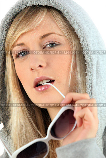Woman in a hooded sweatshirt biting her sunglasses. Стоковое фото, агентство Ingram Publishing / Фотобанк Лори