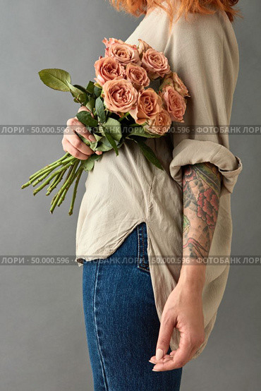 Woman in blue jeans and tatoo hand with a bouquet of beige roses cappuccino on a gray background. Mother’s Day,. Woman in blue jeans with a bouquet of beige roses. Стоковое фото, агентство Ingram Publishing / Фотобанк Лори