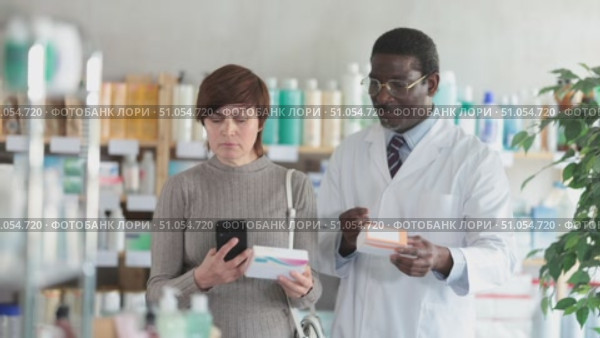 Woman in pharmacy scans QR code on pills, studies item in detail, collects information online, uses quick link to access drugs instructions. African man pharmacist offer available assortment items. Стоковое видео, видеограф Яков Филимонов / Фотобанк Лори