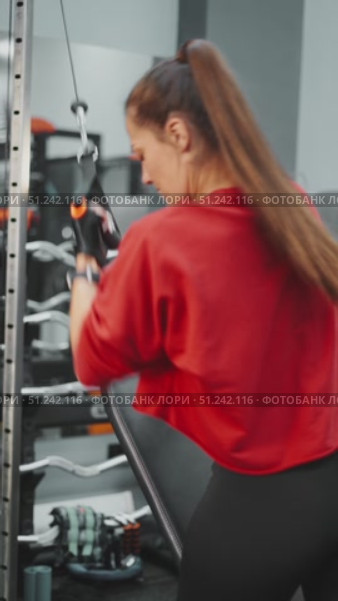 Woman in sports gloves pulling cable machine during workout at gym. Concept of strength training, dedication and building healthy body through discipline and motivation. Стоковое видео, видеограф Енваев Андрей / Фотобанк Лори