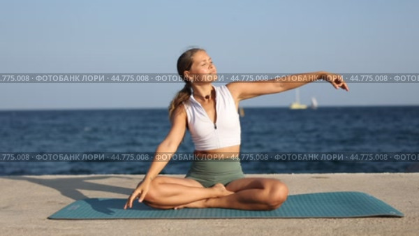 Woman performs half-lotus pose with torso tilted to sides at sea embankment. Стоковое видео, видеограф Яков Филимонов / Фотобанк Лори