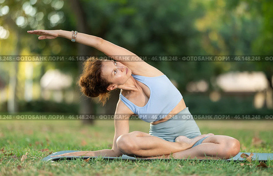 Woman practicing hatha yoga in garden, stretching in an asymmetrical seated asana Parivritta Janu Sirsasana. Стоковое фото, фотограф Яков Филимонов / Фотобанк Лори