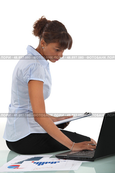 Woman sitting on her desk with a clipboard and laptop. Стоковое фото, агентство Ingram Publishing / Фотобанк Лори