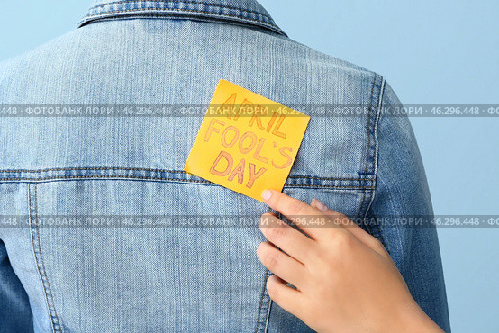 Woman sticking paper to her friend's back against color background, closeup. April Fools' Day prank. Стоковое фото, фотограф Pixel_shot / Фотобанк Лори