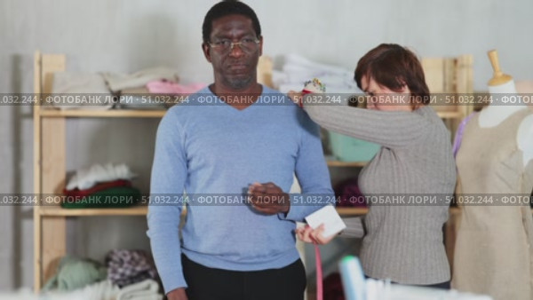 Woman tailor takes measurements from African American man client, using tape measure, measures body size for custom-made dress. Стоковое видео, видеограф Яков Филимонов / Фотобанк Лори