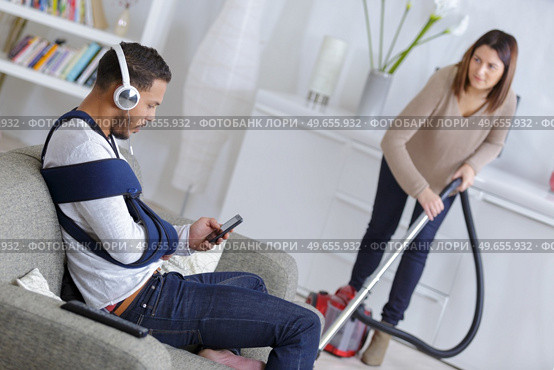 woman vacuuming while man is resting on a couch. Стоковое фото, агентство Ingram Publishing / Фотобанк Лори