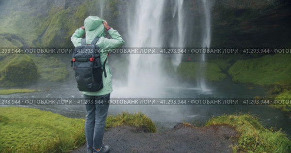 Woman with backpack in front of epic Seljalandsfoss waterfall Iceland. Стоковое видео, видеограф Igor Tichonow / Фотобанк Лори