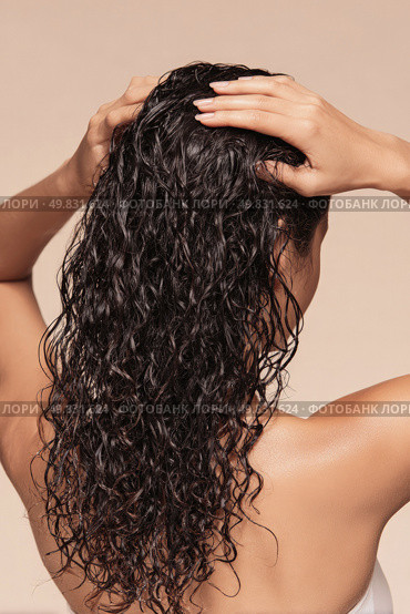 Woman with wet curly hair seen from behind touching scalp gently. Стоковое AI-изображение, AI-художник Катерина Бондарец / Фотобанк Лори