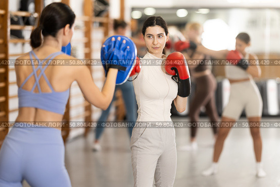 Woman works out strength and speed of boxing punch mitts with help of partner in boxing paws. Стоковое фото, фотограф Яков Филимонов / Фотобанк Лори