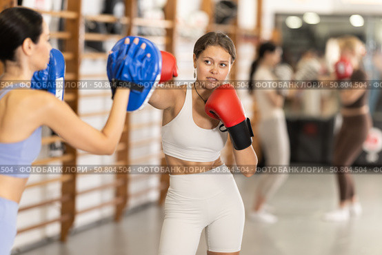 Woman works out strength and speed of boxing punch mitts with help of partner in boxing paws. Стоковое фото, фотограф Яков Филимонов / Фотобанк Лори