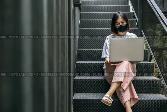 Women wearing masks and playing laptops on the stairs. Selective focus. Стоковое фото, агентство Ingram Publishing / Фотобанк Лори