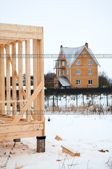 Wood frame house under construction against brick house at winter season. Стоковое фото, фотограф Кекяляйнен Андрей / Фотобанк Лори