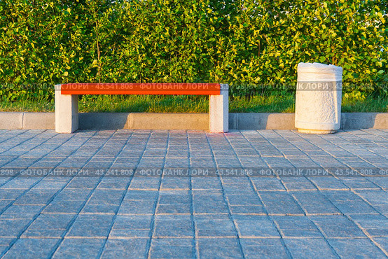 Wooden bench with stone legs and a trash can on the background of a green hedge, illuminated by the evening sun in the park. Стоковое фото, фотограф Михаил Строгалев / Фотобанк Лори