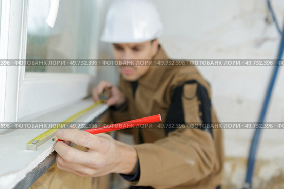 worker measuring glass at a construction site. Стоковое фото, агентство Ingram Publishing / Фотобанк Лори