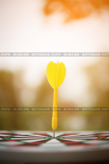 Yellow dart arrow hitting in the center of dartboard. Стоковое фото, агентство Ingram Publishing / Фотобанк Лори