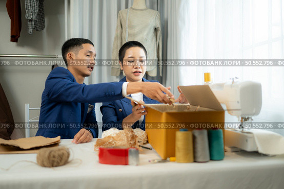 Young Asian businessman and woman Clothes are being packaged for delivery to customers in cardboard boxes and cushioned lump from natural materials that are not toxic to the planet. Стоковое фото, агентство Ingram Publishing / Фотобанк Лори