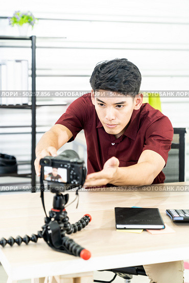 Young asian male blogger setting up camera for recording live vlog video tutorial session at home. IT blogging or vlogging, social media hobby broadcasting, or online learning course concept. Стоковое фото, агентство Ingram Publishing / Фотобанк Лори