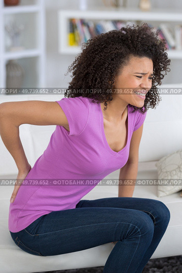 young attractive woman sitting indoor touching aching back. Стоковое фото, агентство Ingram Publishing / Фотобанк Лори