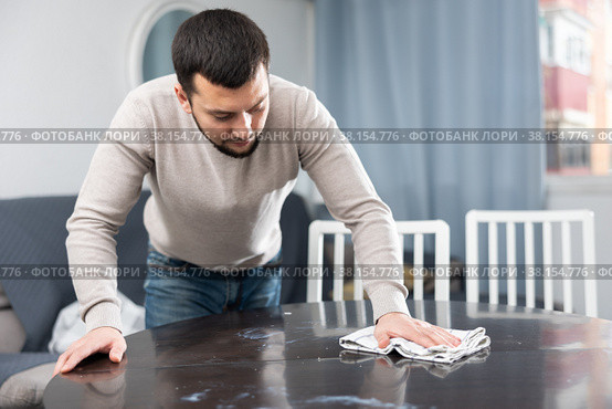 Young bachelor wiping surface of dining table in apartment. Стоковое фото, фотограф Яков Филимонов / Фотобанк Лори
