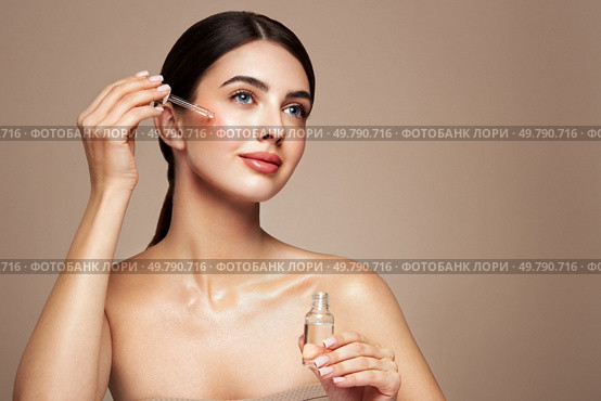 Young beautiful woman applying face serum with pipette. Cosmetic procedures for facial skin care. Стоковое фото, агентство Ingram Publishing / Фотобанк Лори
