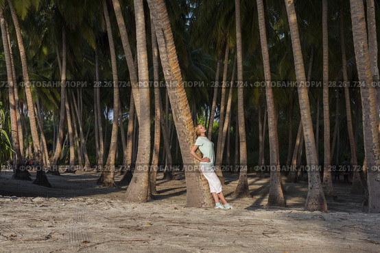 Young beautiful woman standing in a tropical forest leaning on a palm tree. Стоковое фото, фотограф Некрасов Андрей / Фотобанк Лори