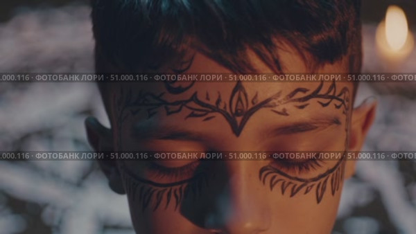 Young child meditating, wearing ceremonial face paint, closed eyes near illuminated candle with ritual white ground markings. Стоковое AI-видео, аниматор Данил Руденко / Фотобанк Лори