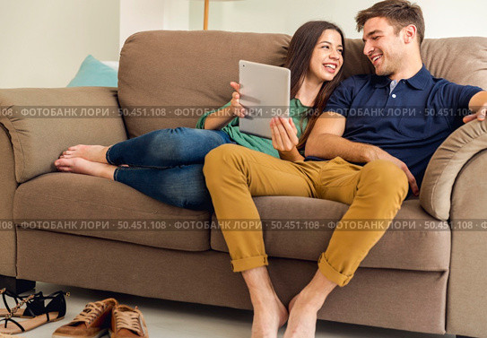 Young couple sitting on the sofa and watching something on a tablet. Стоковое фото, агентство Ingram Publishing / Фотобанк Лори