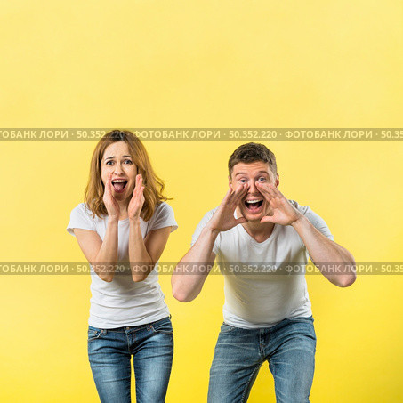 young couple yelling loudly against yellow background. Стоковое фото, агентство Ingram Publishing / Фотобанк Лори